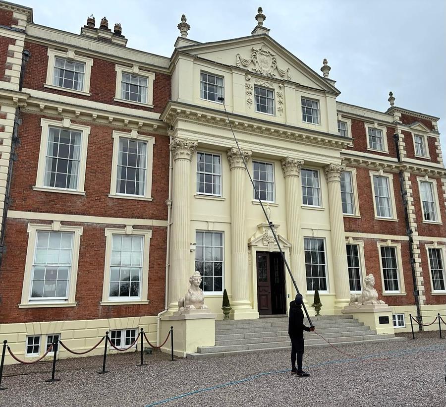TD Exterior Cleaning using a water-fed pole on the sash windows of Hawkstone Hall, a Georgian hall in cream stone and red brick with stone sphinxes beside the entrance steps.