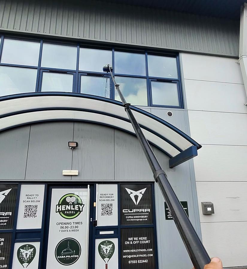 A water-fed pole reaching the upper glazing and curved entrance canopy of the Henley Padel sports club in Shrewsbury.