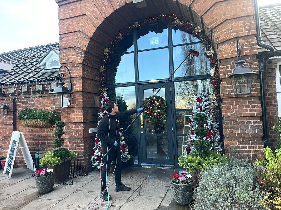Cleaning the glazed brick archway entrance of the Mytton and Mermaid hotel at Atcham near Shrewsbury, decorated with Christmas wreaths and garlands.