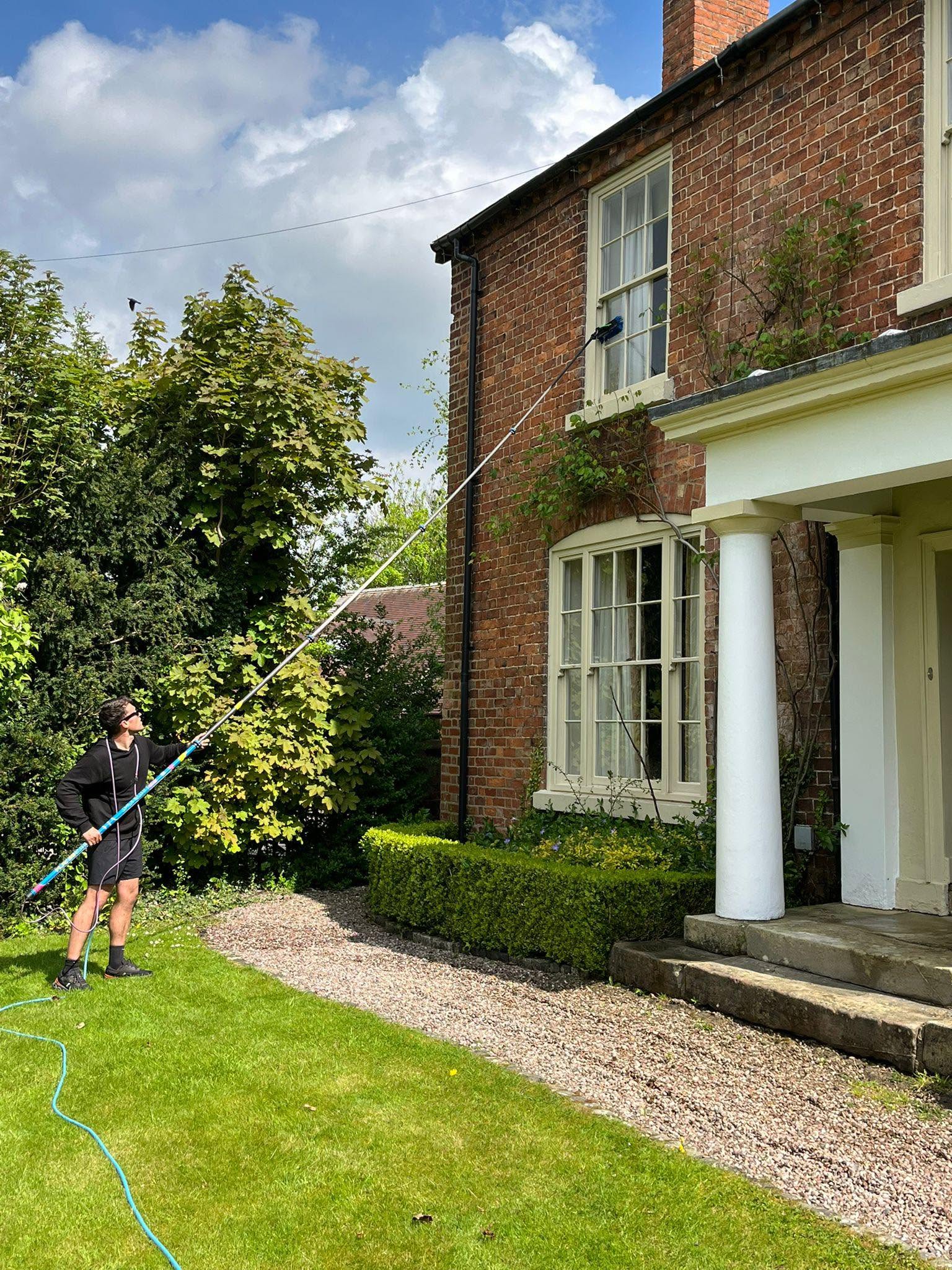 TD Exterior Cleaning operator using a water-fed pole to clean upstairs windows of a red-brick Shropshire house
